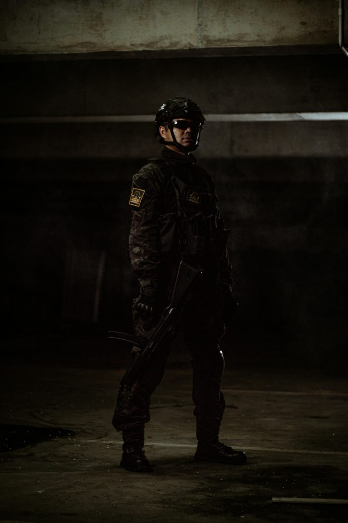 A soldier stands poised with a rifle in a dark, moody setting.